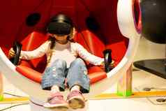 女孩坐着游戏驾驶舱持有比赛操舵轮玩赛车模拟