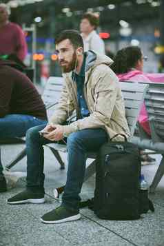 公共运输首选方法旅行完整的长度拍摄英俊的年轻的男人。听音乐手机坐着公共汽车站