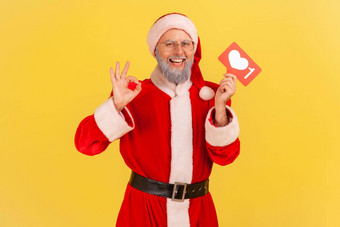 肖像微笑上了年纪的男人。灰色的胡子穿圣诞老人老人服装推荐遵循有趣的博客显示标志