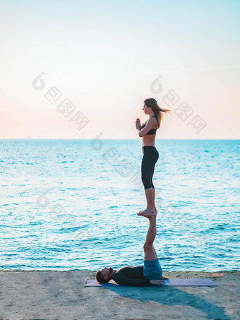 年轻的美丽的夫妇练习爱人瑜伽海海滩水男人。女人日常实践户外自然背景健康的生活方式概念
