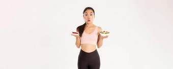 活跃的生活方式健身幸福概念肖像优柔寡断诱人的可爱的亚洲女孩<strong>抵制</strong>诱惑持有美味的蛋糕饮食健康的沙拉