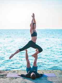 年轻的美丽的夫妇练习爱人瑜伽海海滩水男人。女人日常实践户外自然背景健康的生活方式概念