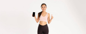 <strong>体育运动</strong>技术活跃的生活方式概念满意微笑亚洲健身女孩有吸引力的女运动员显示竖起大拇指智能<strong>手机</strong>屏幕推荐移动锻炼跟踪器应用程序