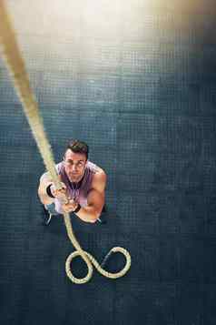 爬冠军肌肉发达的年轻的男人。攀爬绳子健身房