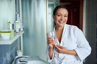 迷人的女人白色浴袍微笑快乐的露出牙齿的微笑站玻璃矿物水浴室