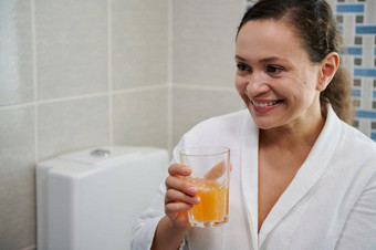 中年女人浴袍持有玻璃水冒泡的平板电脑需要每天剂量维生素矿物质