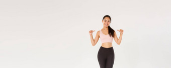 完整的长度专业健身教练亚洲女孩阿塞尔特指出微笑快乐锻炼健身房获得完美的身体培训穿运动服装白色背景