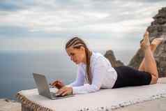 女人说谎打字移动PC键盘阳台美丽的海视图穿白色上衣黑色的裙子自由旅行假期概念数字游牧