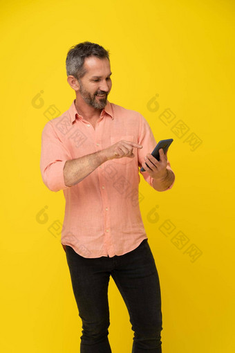 中间岁的灰色头发的英俊的适合男人。持有智能<strong>手机</strong>穿桃子衬衫孤立的黄色的成熟的肌肉男人。电话应用程序广告