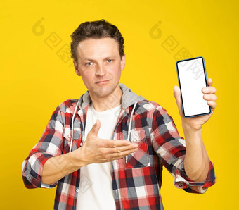 应用程序网站介绍持有智能手机白色屏幕金发碧眼的男人。穿红色的格子衬衫男人。电话显示模拟孤立的黄色的背景移动应用程序广告