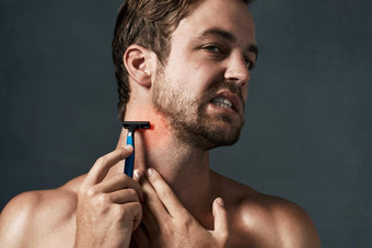 剃须养生法导致问题英俊的年轻的男人。扮鬼脸剃须