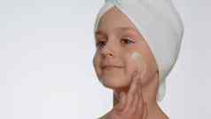 可爱的年轻的孩子女孩应用清洗保湿脸奶油护肤品自然噪音化妆品
