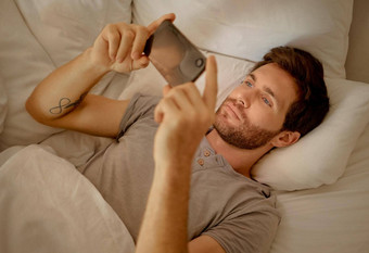 年轻的男人。放松床上电话看电影系列在线社会媒体视频应用程序浏览互联网新闻技术手机智能手机玩游戏卧室