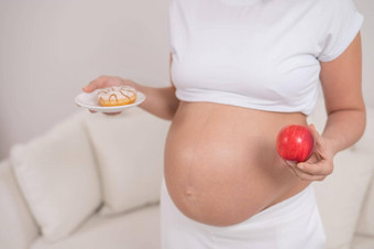 怀孕了女人持有红色的苹果甜甜圈选择食物