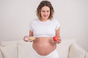 怀孕了女人持有红色的苹果甜甜圈选择食物