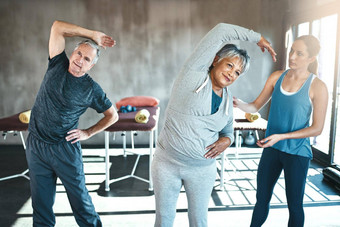 激活健康的退休加入健身房高级男人。女人工作教练