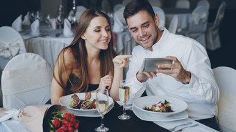 快乐有吸引力的年轻的人看智能手机微笑会说话的晚餐<strong>餐厅</strong>现代技术浪漫概念