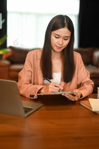 迷人的亚洲女人坐着前面移动PC数字平板电脑首页办公室