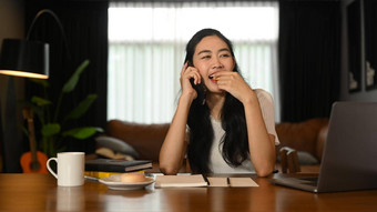 快乐的年轻的女人愉快的电话谈话朋友坐着舒适的首页办公室