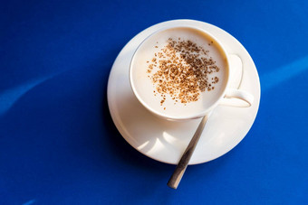 卡布奇诺咖啡蓝色的背景白色杯勺子咖啡豆子早....咖啡意大利传统的意大利早餐小白色陶瓷杯咖啡科普兹空间