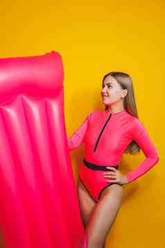 年轻的纤细的女人粉红色的泳衣黄色的背景女孩充气床垫游泳池夏天假期