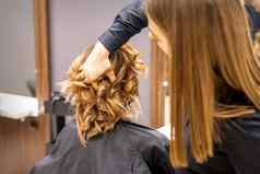 女理发师检查棕色（的）卷曲的发型年轻的高加索人女人美沙龙