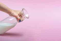 壶牛奶粉红色的背景女人的手牛奶玻璃瓶空间文本大横幅