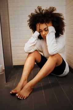 压力累了精神健康年轻的黑色的女人坐着浴室地板上淋浴首页头疼抑郁症焦虑女伤心悲伤恐惧倦怠