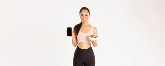 体育运动幸福活跃的生活方式概念微笑苗条的可爱的亚洲健身女孩<strong>健身房</strong>教练显示沙拉智能手机屏幕推荐下载饮食跟踪器<strong>卡</strong>路里提醒