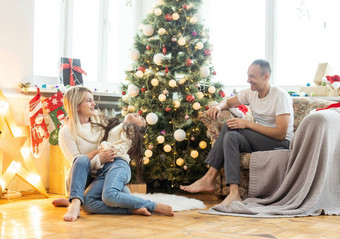 美丽的年轻的家庭享受假期时间装修圣诞节树安排圣诞节灯有趣的