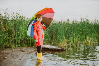 男孩红色的雨衣黄色的橡胶靴子站河银行持有彩虹伞学校孩子站秋天湖孩子穿防水衣服<strong>岸上</strong>的