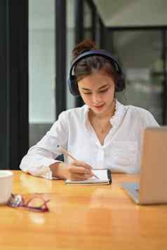 集中女学生穿耳机听讲座研究在线移动PC使笔记笔记本