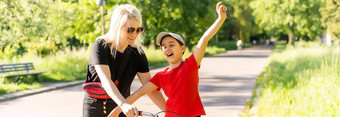美丽的快乐年轻的妈妈。教学女儿骑自行车微笑夏天公园背景