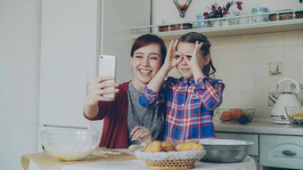 微笑<strong>妈妈</strong>。有趣的女儿采取自拍照片智能手机相机使愚蠢的脸烹饪首页<strong>厨房</strong>家庭烹饪人概念