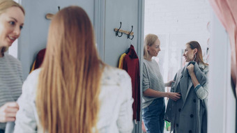漂亮的年轻的女人检查时尚外套拟合房间朋友帮助评价服装会说话的手势服装