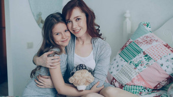 肖像可爱的微笑女孩拥抱快乐妈妈。相机坐着床上明亮的卧室首页