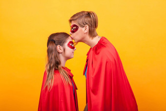妈妈。超人服装接吻女孩额头黄色的背景