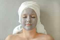 年轻的女人粘土面具脸毛巾头形式头巾谎言关闭眼睛享受水疗中心治疗面部皮肤护理脸特写镜头前视图