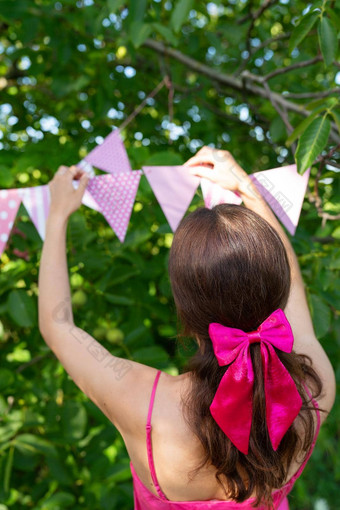 女孩挂起三角旗帜粉红色的颜色背景绿色花园女孩粉红色的衣服弓头发节日装饰庆祝活动概念