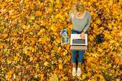 可爱的女人移动PC秋天公园美自然场景色彩斑斓的树叶背景黄色的树叶子秋天季节秋天户外生活方式快乐微笑女人秋天叶子