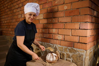 愉快的女人贝克白色酋长帽黑色的围裙把小麦小穗表格新鲜的烤面包