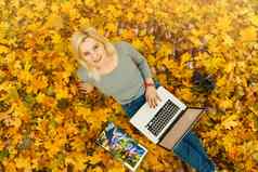 可爱的女人移动PC秋天公园美自然场景色彩斑斓的树叶背景黄色的树叶子秋天季节秋天户外生活方式快乐微笑女人秋天叶子