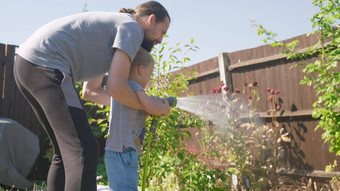 父亲儿子有趣的男孩浇水草坪上植物花园住房后院爸爸夏天房子工作勤劳的学前教育孩子在户外孩子们做家务活动孩子们