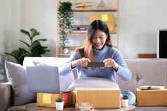 亚洲女人拍摄包裹盒子智能手机交付货物客户在线互联网开始小业务主人的电子商务概念