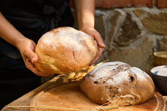 细节贝克手持有轮面包面包木董事会新鲜的烤自制的黑麦面包小麦耳朵