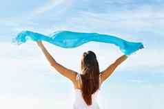 年轻的女人持有蓝色的围巾天空后视图图像年轻的女人持有蓝色的围巾天空