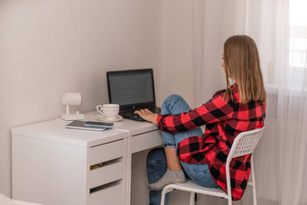 欧洲专业女人坐着移动PC首页办公室桌子上积极的女人研究工作穿红色的格子衬衫牛仔裤
