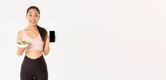 <strong>体育运动</strong>幸福活跃的生活方式概念微笑苗条的可爱的亚洲健身女孩健身房教练显示沙拉智能<strong>手机</strong>屏幕推荐下载饮食跟踪器卡路里提醒