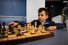 可爱的聪明的高加索人孩子男孩坐着表格玩国际象棋移动国际象棋一块棋盘