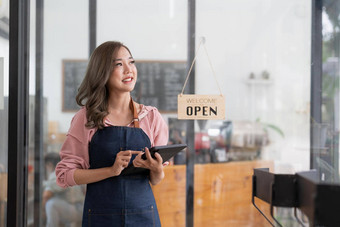 年轻的亚洲女人咖啡商<strong>店老板</strong>穿围裙持有数字平板电脑准备好了收到订单